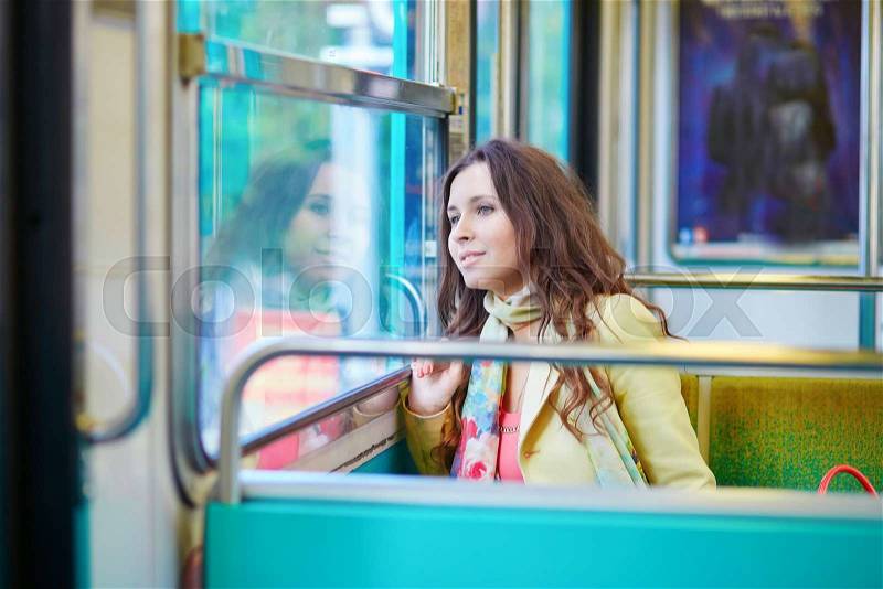 Beautiful young woman travelling in a train of Parisian subway and looking through the window, stock photo