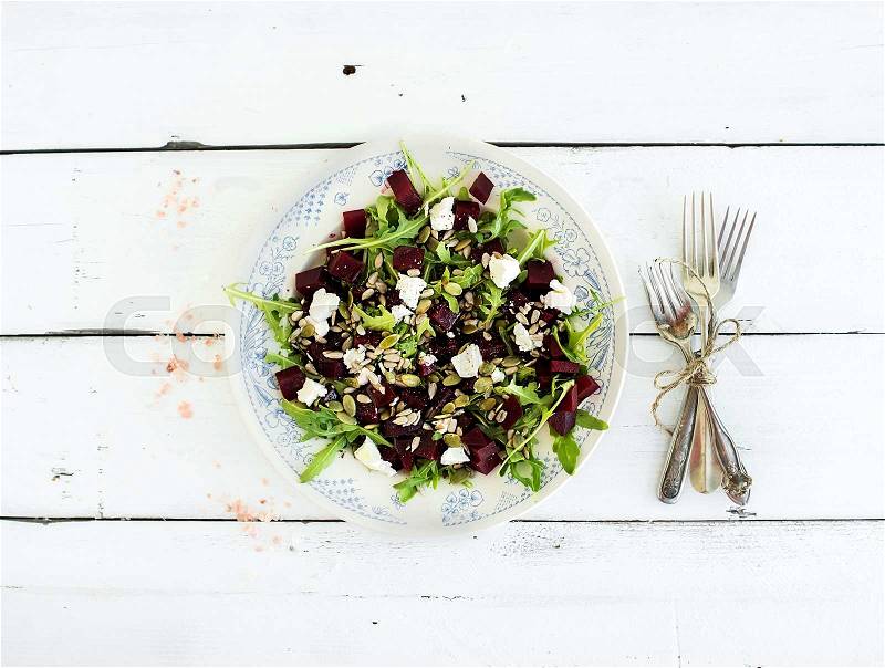 Beetroot salad with arugula, feta cheese, red salt and pumpkin seeds in vintage plate over white rustic wooden background, top view, stock photo