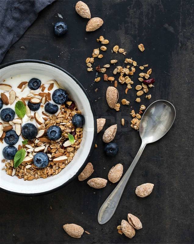 Healthy breakfast. Oat granola with fresh blueberries, almond, yogurt and mint in a rustic metal bowl over dark grunge surface. Top view, stock photo