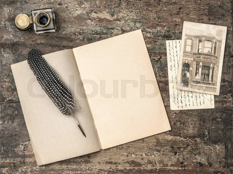 Open book, vintage writing tools feather pen and inkwell on textured wooden background. Retro style toned picture, stock photo