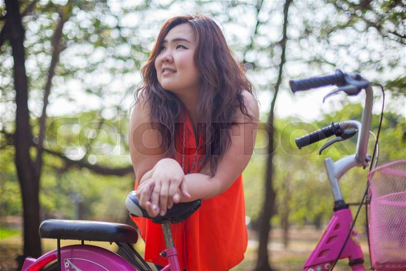 Happy fatty asian woman posing with bicycle outdoor in a park, stock photo