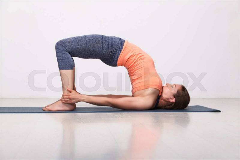 Beautiful sporty fit yogini woman practices yoga asana setu bandhasana - bridge pose advanced variation in studio, stock photo