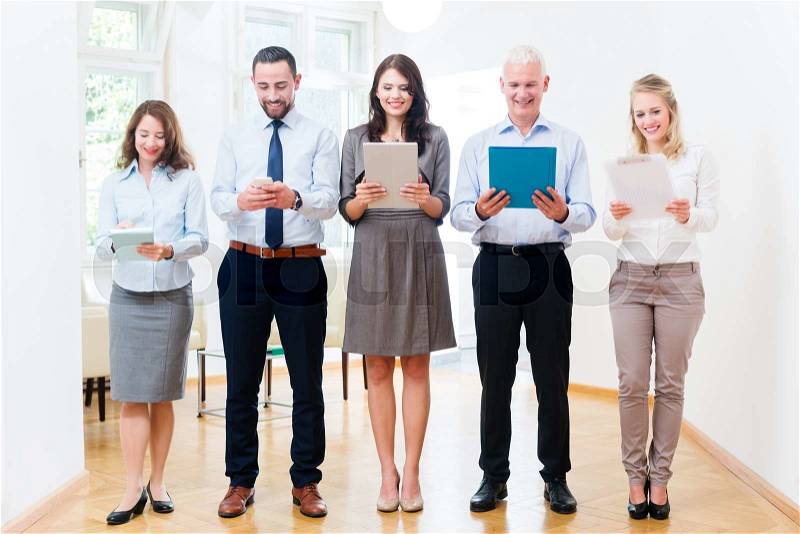 Concept - business people in office standing in row with phone, tablet computer, and file, stock photo