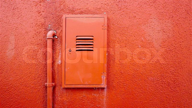 Metal pipe and electric box on orange color wall in Burano, Venice, Italy, stock photo
