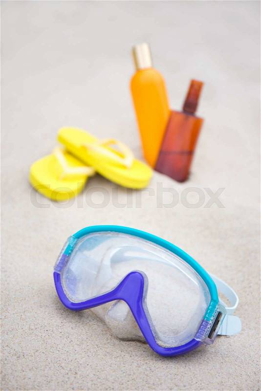 Diving concept - mask, slippers and suntan lotion bottles in white sand, stock photo