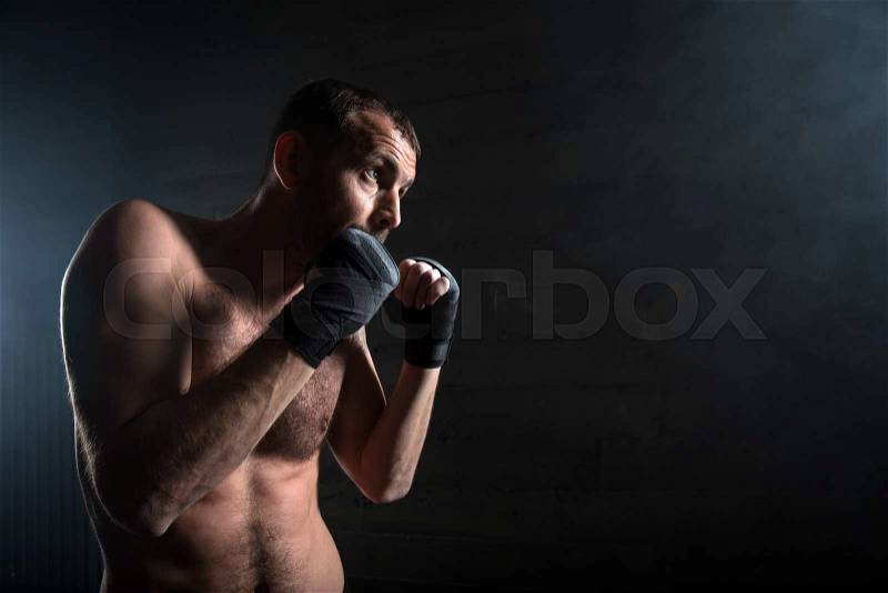 Young boxer in light weight with bare-chested in fighting stance against a dark background in the studio, stock photo