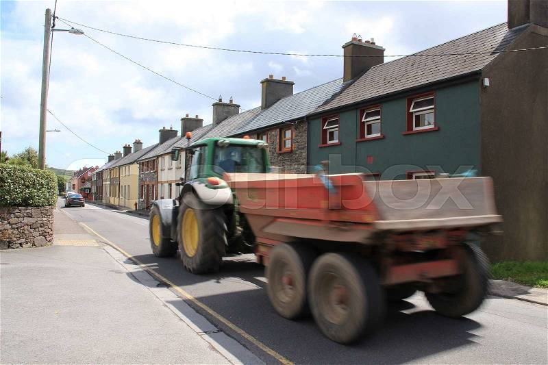The tractor with an empty trailer is driving through the streets of the harbour Dingle in Ireland in the summer, stock photo