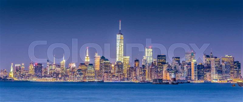 New York City Manhattan downtown skyline at dusk with skyscrapers illuminated over Hudson River panorama. Horizontal composition, copy space, stock photo
