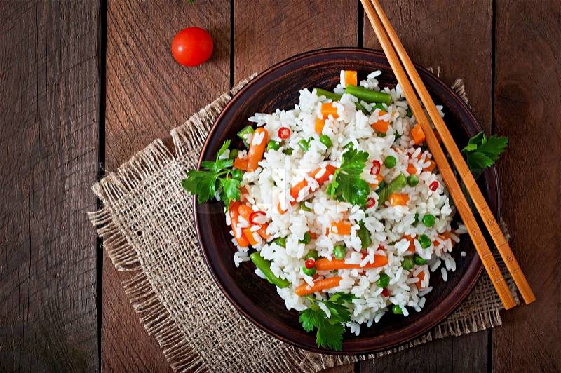 Appetizing healthy rice with vegetables in a ceramic dish on a wooden background, stock photo