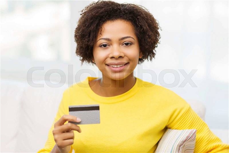 People, bank, shopping and e-money concept - happy african american young woman sitting on sofa with credit or debit card at home, stock photo