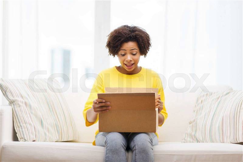 People, delivery, shipping and postal service concept - happy african american young woman opening cardboard box or parcel at home, stock photo