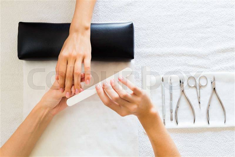 Lady receiving a manicure in a salon having her fingernails filed by a professional manicurist, view from above of their hands and tools, stock photo