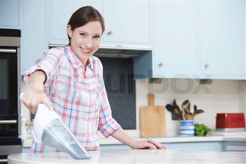 Woman Cleaning Kitchen Using Hand Held Vacuum Cleaner, stock photo