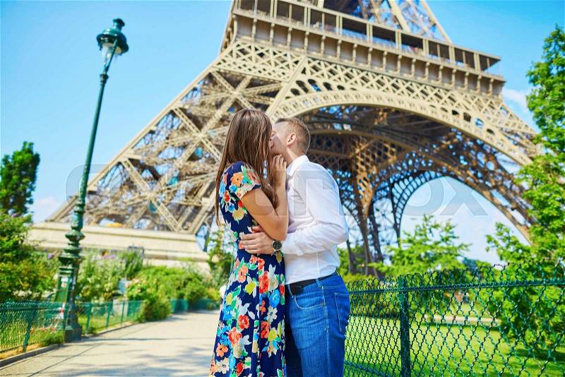 Young romantic couple kissing with passion near the Eiffel tower in Paris, France, stock photo
