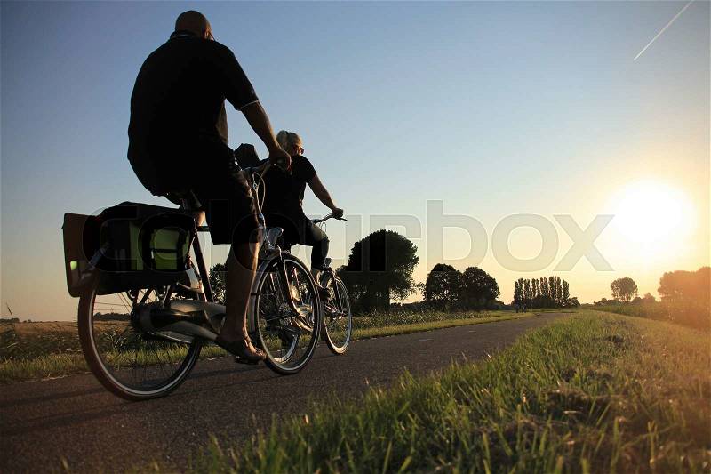 Couple, man and wife, biking on the cycle path at the country side at sunset in the summer, stock photo