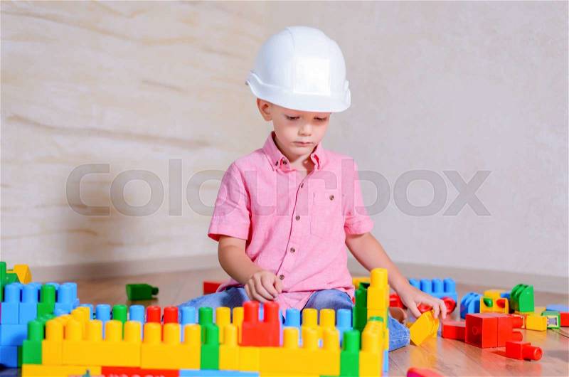 Creative young boy playing with a collection of multicolored building blocks wearing a hardhat as he pretends to be an architect or engineer, stock photo