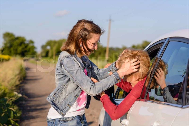Two women fighting at the roadside on a rural road with one inside and one outside the car fighting through the open drivers window, stock photo