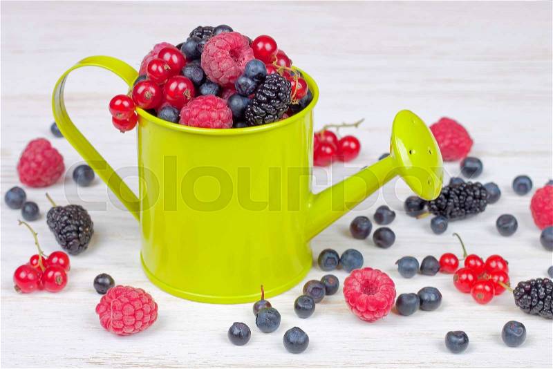 Mixed berries in a small light green decorative watering can on white wooden background, stock photo