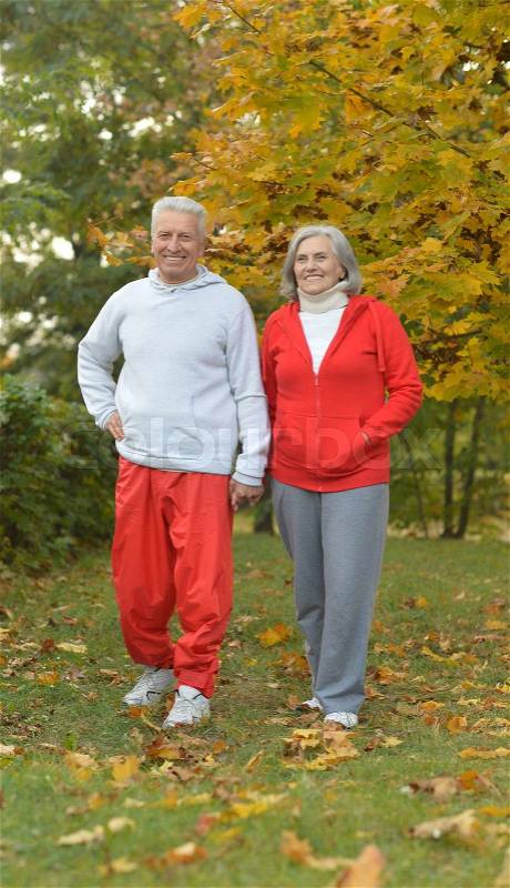 Happy fit senior couple walking in autumn park, stock photo