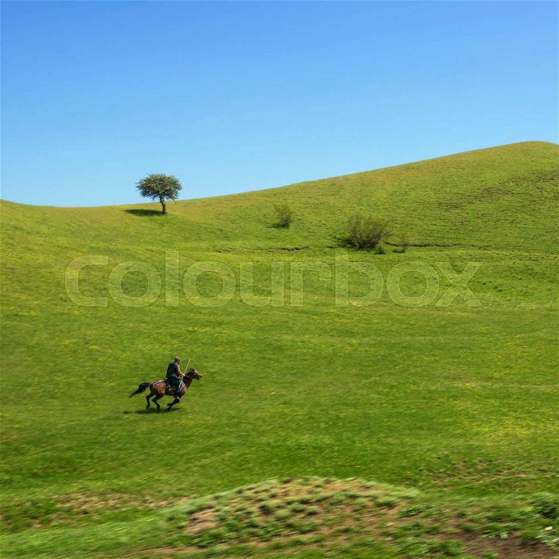 A man on horseback galloping fast across the hills, stock photo
