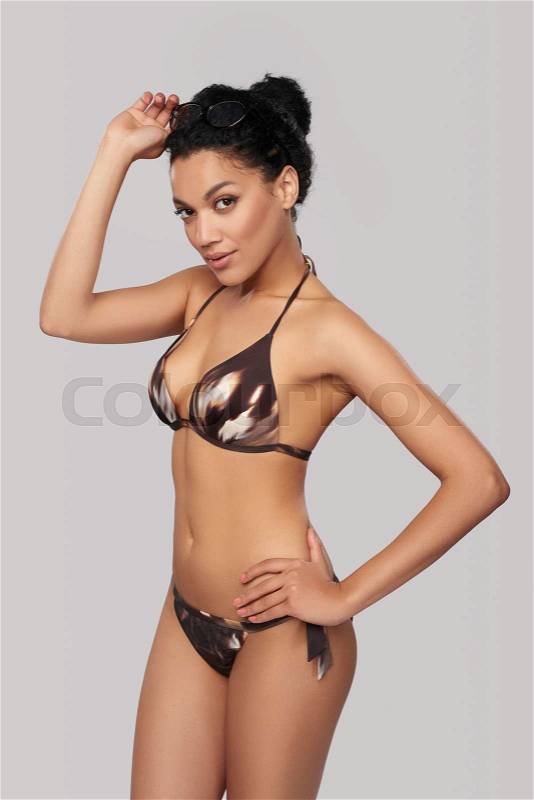 Fashionable mixed race african american - caucasian woman in brown swimsuit and leopard print glasses posing holding glasses rim, stock photo