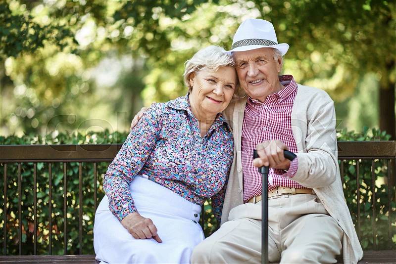 Senior couple sitting on bench in park and looking at camera, stock photo