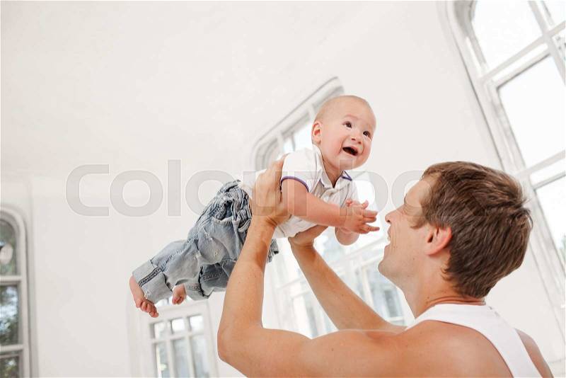Young smiling father with his nine months old son playing at home on white home background. father throwing up his son, stock photo