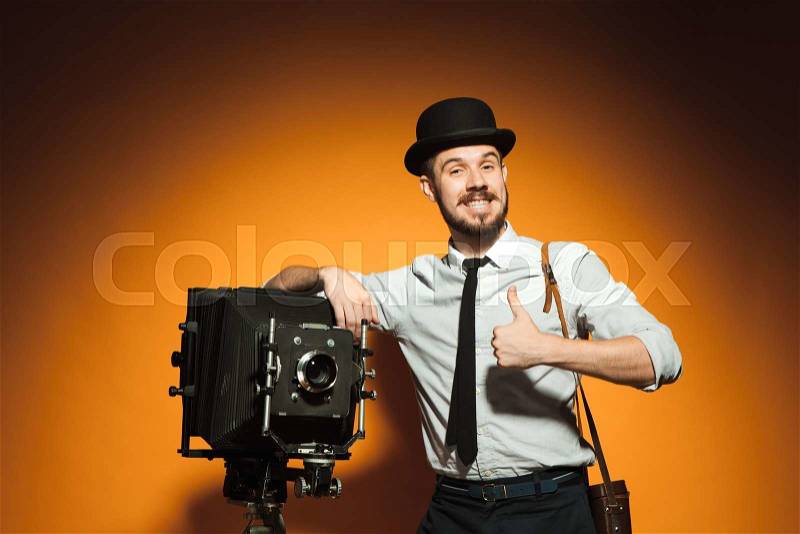 Young smiling man in hat as photographer with retro camera on an orange background, stock photo