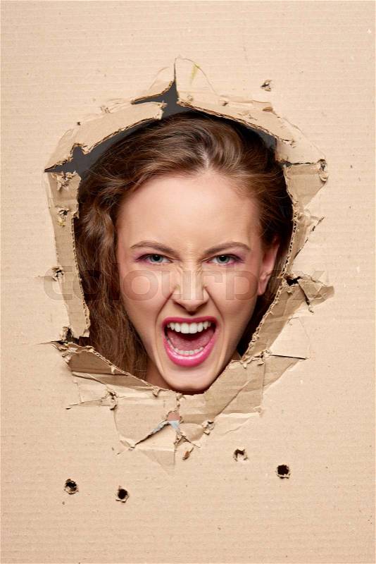 Emotional screaming girl peeping through hole in paper, stock photo