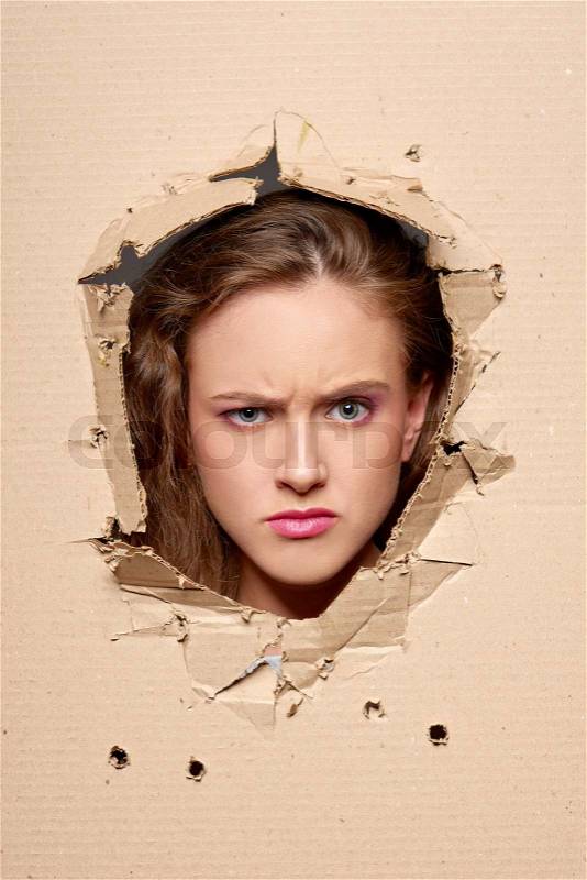 Displeased girl peeping through hole in paper, stock photo