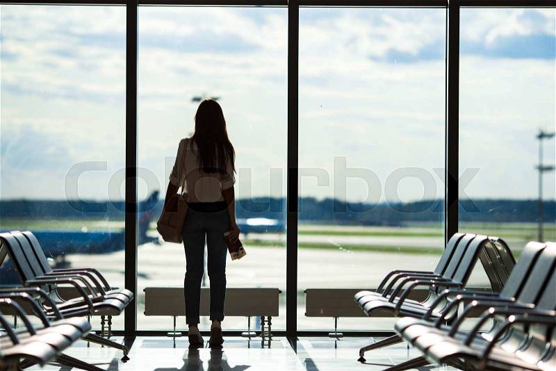 Silhouette of passenger in an airport lounge waiting for flight aircraft, stock photo