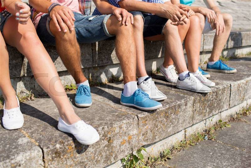 Friendship, leisure, summer and people concept - close up of friends legs sitting on city square, stock photo