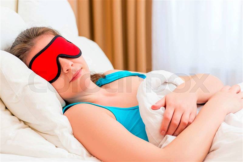 A woman with eye mask sleeping under a blanket, stock photo