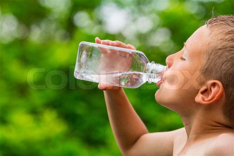 Closeup of young boy drinking pure tap water from transparent plastic drinking bottle while outdoors on a hot summer day, stock photo