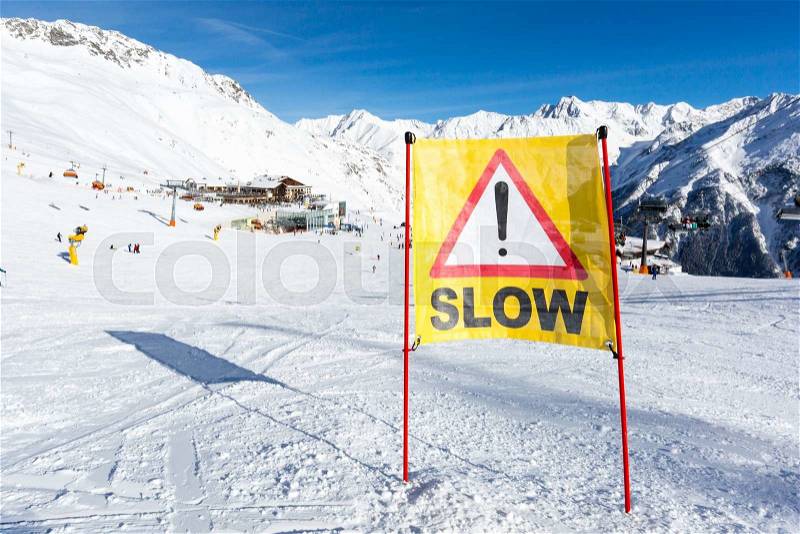 Yellow slow down warning sign placed in the snow on the piste at the ski resort Soelden in Austria, stock photo