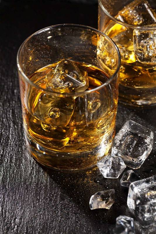 Glasses of scotch whiskey with ice on black stone table, stock photo