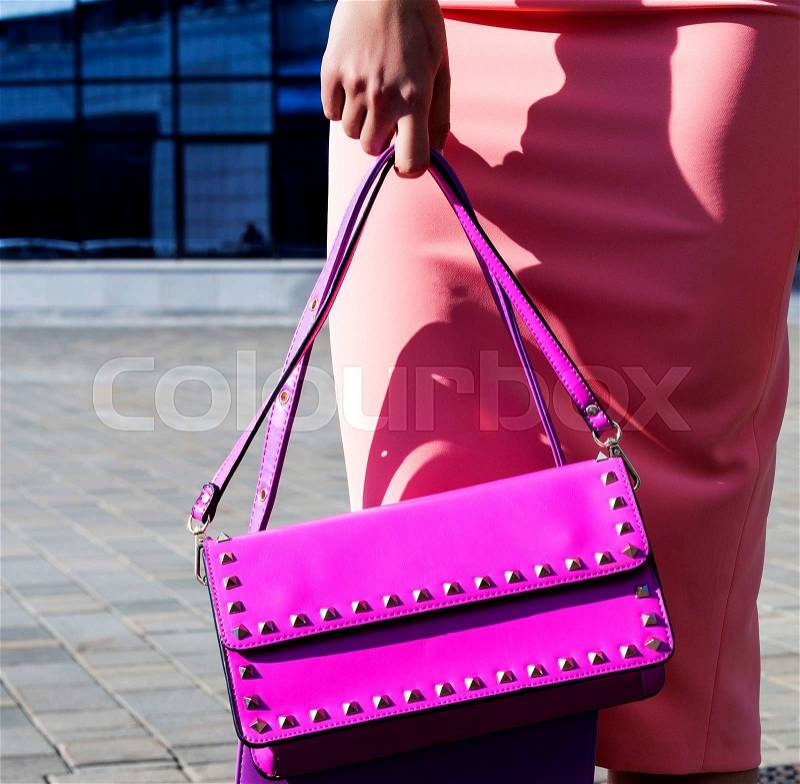 Fashion model with clutch in pink dress poses outdoors, stock photo