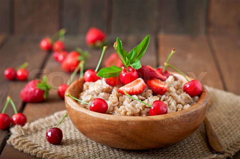 Oatmeal porridge with berries in a wooden bowl, stock photo