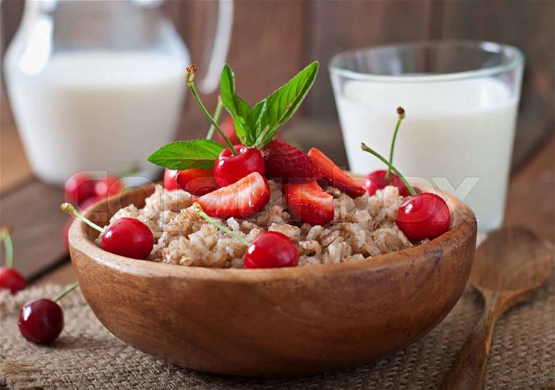 Oatmeal porridge with berries in a wooden bowl, stock photo