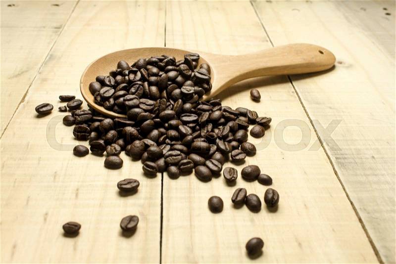 Coffee crop beans on spoon and wooden background, stock photo