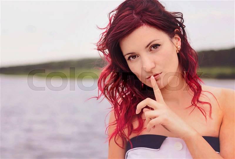 Secret woman. Female showing hand silence sign, natural outdoor background, stock photo