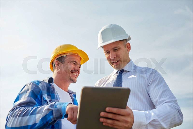 Business, building, teamwork, technology and people concept - smiling builders in hardhats with tablet pc computer outdoors, stock photo