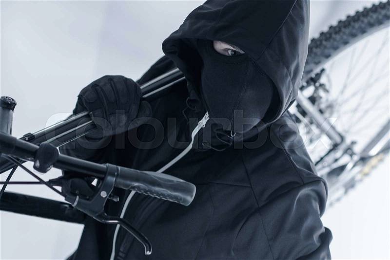 Bike Theft. Bike Thief in a Hood, Black Mask and Black Gloves. Caucasian Male Thief, stock photo