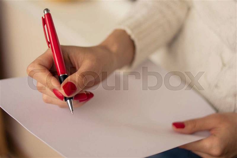 Female hands with red nails write on a sheet of paper, stock photo