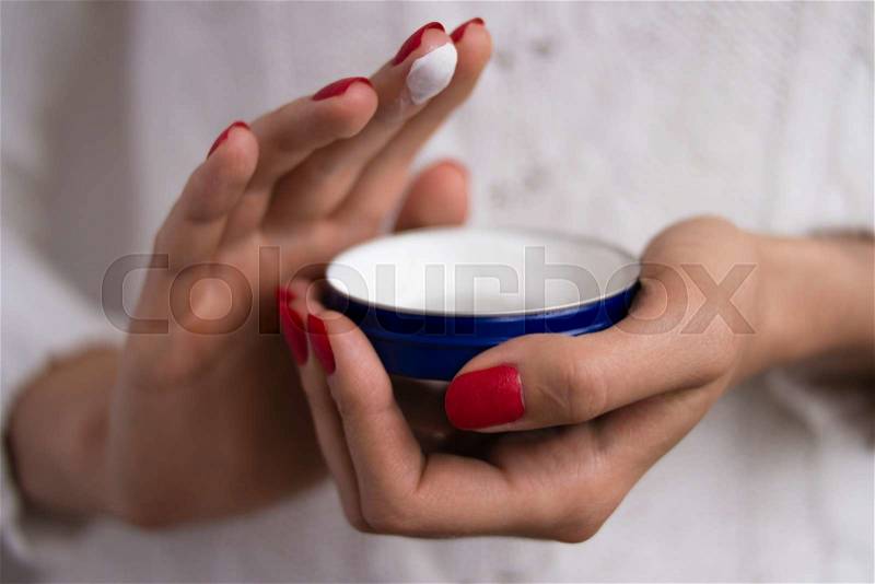 Female hands with red nails applied the cream out of the blue jar, stock photo