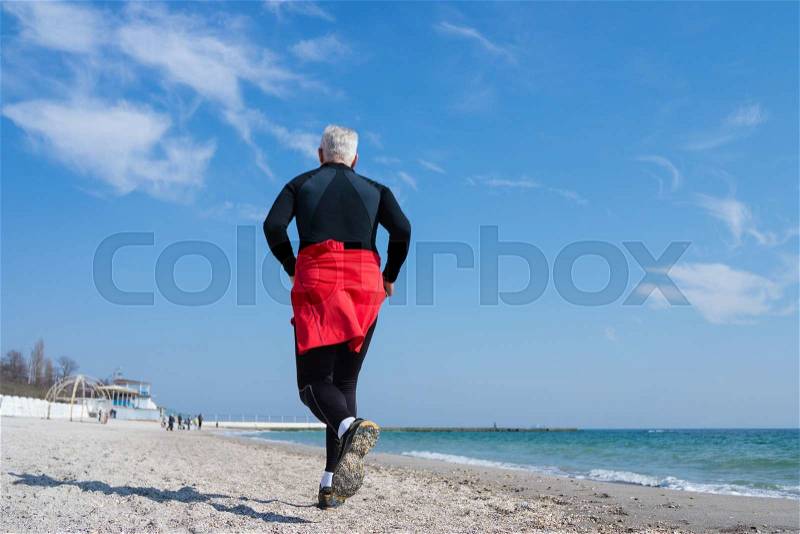 Gray-haired man runs along the beach tracksuit, stock photo