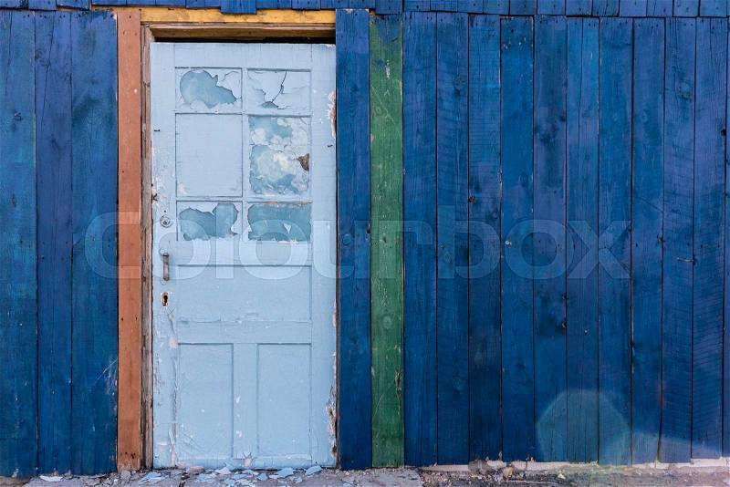 Old wooden light blue door in a dark blue wall. Wooden colored building. Abandoned condition. Boards are painted in different colors, stock photo