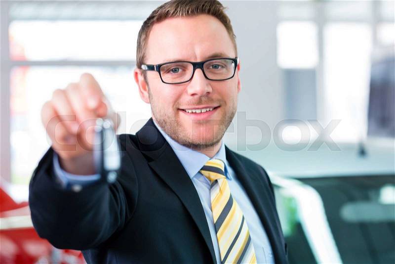 Salesman handing over auto key at car dealership, stock photo