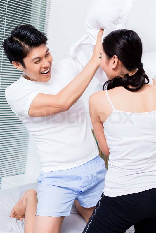 Chinese Woman and man having pillow fight, stock photo