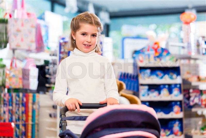 Little girl playing with baby doll carriage in toy store, stock photo